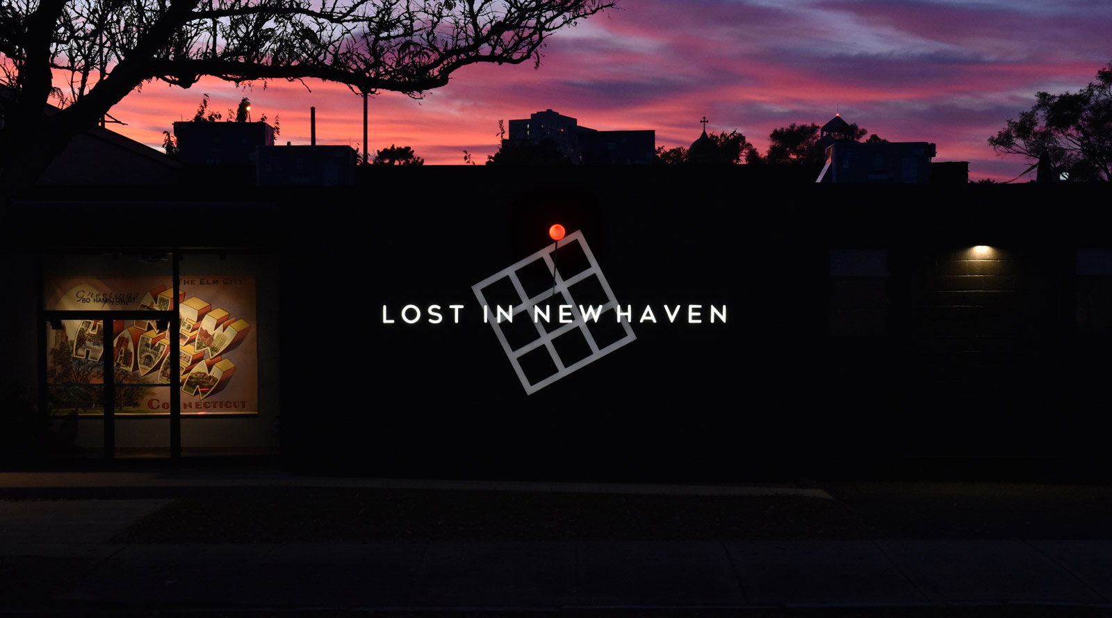 Lost In New Haven illuminated signage at sunset with red map pin glowing above the grid element.